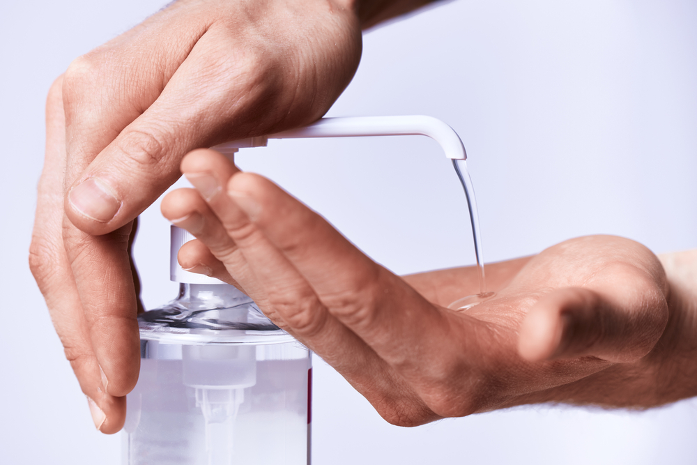  Jeune femme qui utilise un flacon doseur de gel hydroalcoolique et applique une dose de produit sur ses mains.